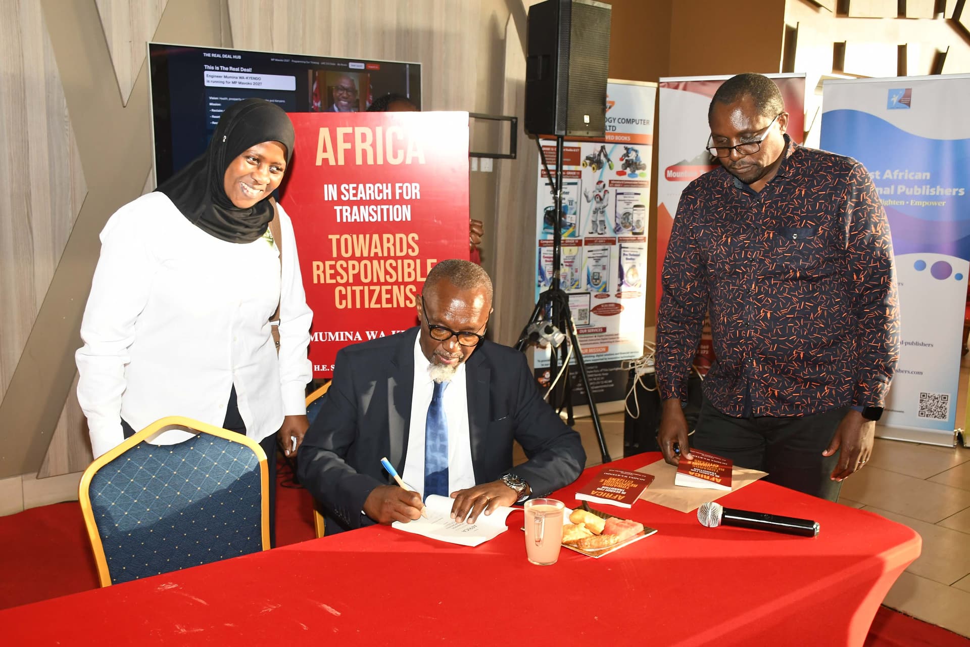 Readers watching as Eng. Mumina Wa-Kyendo signs their copies
