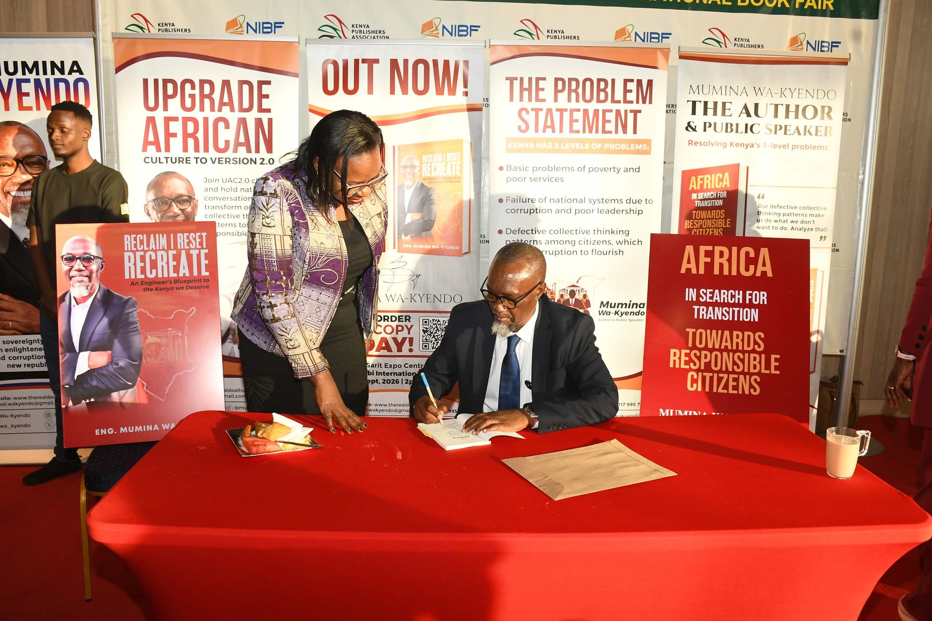 Eng. Mumina Wa-Kyendo signing a book in front of the launch banners